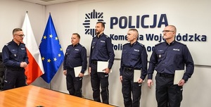 Sala odpraw na wprost stoi czterech funkcjonariuszy, po lewej stronie stoi Komendant Wojewódzki Policji w Łodzi, po prawej kadra kierownicza Komendy Wojewódzkiej Policji w Łodzi.