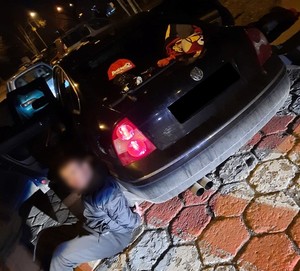 Jeden z zatrzymanych mężczyzn siedzi na ziemi oparty o samochód