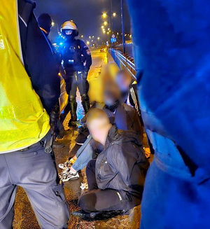 Policjanci umundurowani pilnują zatrzymanych pseudokibiców