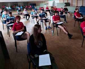 uczniowie siedzą na krzesłach na sali rozwiązują testy