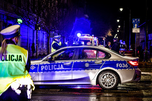 radiowóz oznakowany stojący bokiem, obok policjant