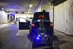 Robot policyjny wyciąga pakunek z bagażnika samochodu