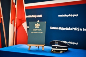Na stole stoi Konstytucja Rzeczypospolitej Polskiej obok niej leży czapka policyjna.