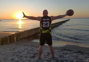 Mężczyzna stoi na plaży, trzyma piłkę do koszykówki.