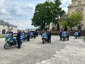 Plac, policjanci w galowych mundurach stoją przy motocyklach.
