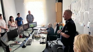 Policjant stoi za pulpitami monitoringu, po drugiej stronie stoją studenci.
