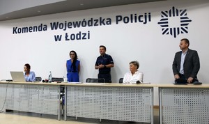 Sala odpraw, za stołem siedzą prelegenci na ścianie napis Komenda Wojewódzka Policji w Łodzi.