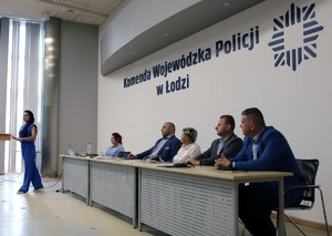 Sala odpraw, za stołem siedzą prelegenci na ścianie napis Komenda Wojewódzka Policji w Łodzi.