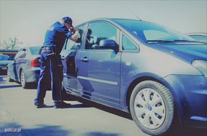 Policjant zagląda do samochodu stojącego na parkingu.