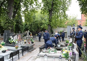 Policjanci kładą znicze na grobie, za nimi delegacja kierownictwa garnizonu łódzkiego.