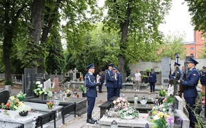 Cmentarz, policjanci trzymają znicze stoją przed grobem.