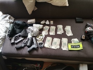 Na stole leżą banknoty, broń, dżokejka, opaska z napisem Policja.