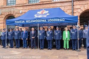 Zaproszeni goście stoją pod namiotem z napisem Komenda Wojewódzka Policji w Łodzi.