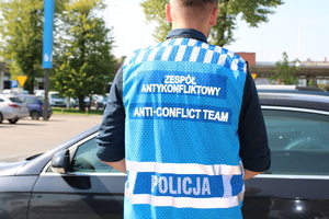 policjant stoi tyłem, w niebieskiej kamizelce z napisem zespół antykonfliktowy.