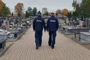 Umundurowani policjanci idą alejką na cmentarzu.
