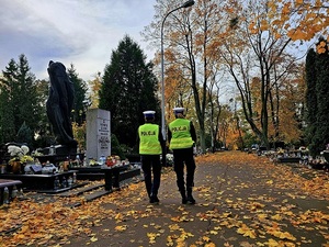 Policjanci idą uliczkami cmentarza.