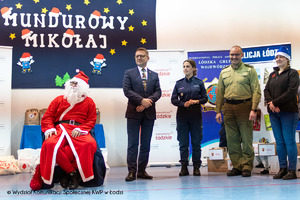 Mikołaj siedzi na krześle obok policjant i zaproszeni goście.