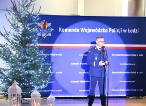 Komendant Wojewódzki Policji w Łodzi stoi przy mikrofonie, obok choinka.
