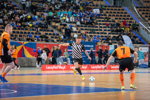 Zdjęcie przedstawia zawodników podczas meczu w piłkę halową, w tle widownia.