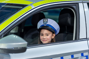 Dziewczynka w policyjnej czapce siedzi w radiowozie.