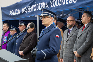 Komendant Wojewódzki Policji w Łodzi przemawia przy mikrofonie z tyłu namiot pod którym stoją zaproszeni goście.