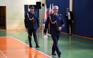 Komendant Wojewódzki Policji w Łodzi maszeruje przez środek sali , za nim dowódca uroczystości.