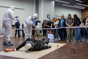 Symulacja miejsca zdarzenia, policjanci w kombinezonach w trakcie oględzin.