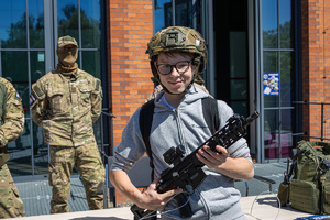 Nastolatek w kasku stoi z pistoletem maszynowym, w tle policyjny kontrterrorysta.