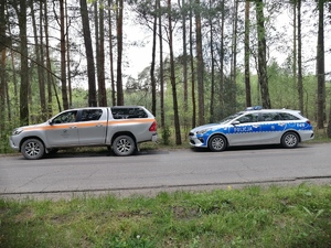 Radiowóz policyjny oraz pojazd straży leśnej.