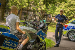 Chłopczyk na motocyklu w tle policjantka.