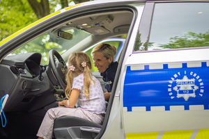 Dziewczynka siedzi za kierownicą w radiowozie obok policjantka.