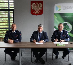 Komendanci z Komendy Wojewódzkiej Policji w Łodzi i prezes Zarządu Wojewódzkiego Funduszu Ochrony Środowiska i Gospodarki Wodnej siedzą za stołem i podpisują porozumienie.