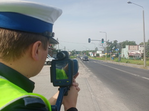 policyjna akcja ,,kierujący-pieszy&quot;, policjant kontroluje prędkość kierowców zbliżających się do przejścia dla pieszych.