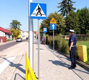 Policjant Ruchu Drogowego stoi przy przejściu dla pieszych w okolicy szkoły, widać znak &quot;Agatka&quot;.