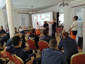 Dwaj policjanci mają założone alkogoogle, inni policjanci siedzą na krzesłach.