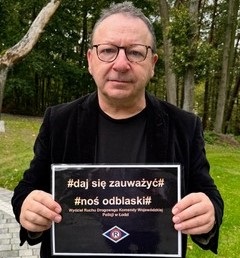 Mężczyzna trzyma kartkę z czarnym tłem z napisem #daj się zauważyć # nos odblaski.