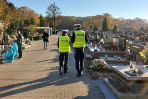 policjanci idą cmentarną alejką.