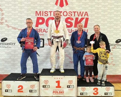 Podium, mężczyźni na podium, na 3 miejscu stoi mężczyzna z dwójką dzieci.