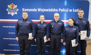 Policjanci stoją na ściance z aktami mianowania.