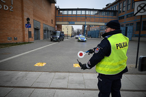 Policjant w kamizelce odblaskowej z napisem policja kieruje ruchem.