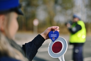 policyjna akcja ,,jak kocha to poczeka&quot;, na zdjęciu policjantka trzyma serduszko  natle tarczy do zatrzymywania pojazdów.