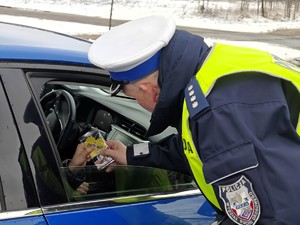 policjant wręcza kierowcy serduszko z akcji profilaktycznej ,,jak kocha to poczeka&quot;.