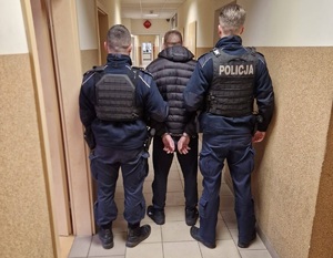 Umundurowani policjanci stoją z zatrzymanym mężczyzną.