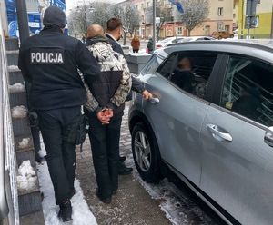 Policjanci w cywilu z zatrzymanym stoją przy samochodzie.