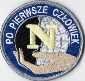 Naszywka policyjna w kształcie koła, dłoń trzymająca literkę N.Napis po pierwsze człowiek