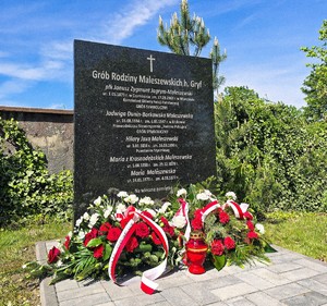 Tablica pamiątkowa i kwiaty na dole.