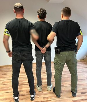 Policjanci w cywilu stoją z zatrzymanym.