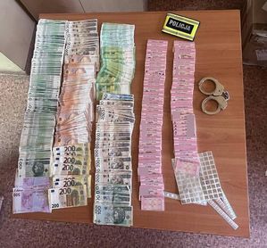 Opaska odblaskowa z napisem Policja, obok poukładane banknoty i dowody osobiste, kajdanki.