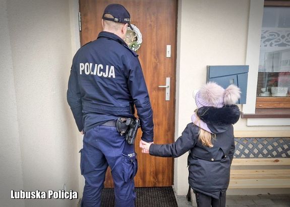 Policjant trzyma dziecko za rękę.
