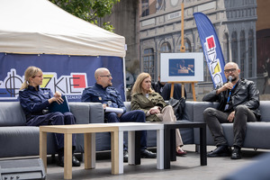 Eksperci siedzą na kanapach podczas debaty, przed nimi stoliki.